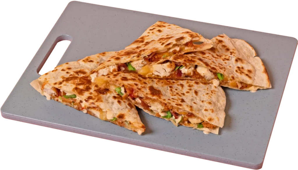 Four toasted, triangular quesadilla slices stacked on a gray cutting board, showing a filling of crispy chicken, melted cheese, bacon, and chopped green onions with a creamy sauce drizzle.