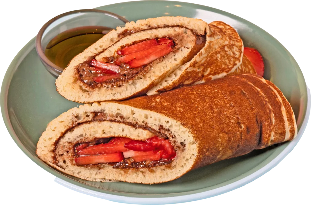 Two halves of a dessert burrito made with a folded pancake, filled with chocolate spread and sliced strawberries, served on a green plate with a side of syrup.