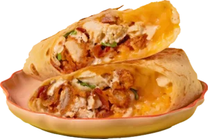 Two halves of a toasted breakfast burrito stacked on a peach-colored plate, filled with crispy chicken, scrambled eggs, melted cheese, and bacon bits.